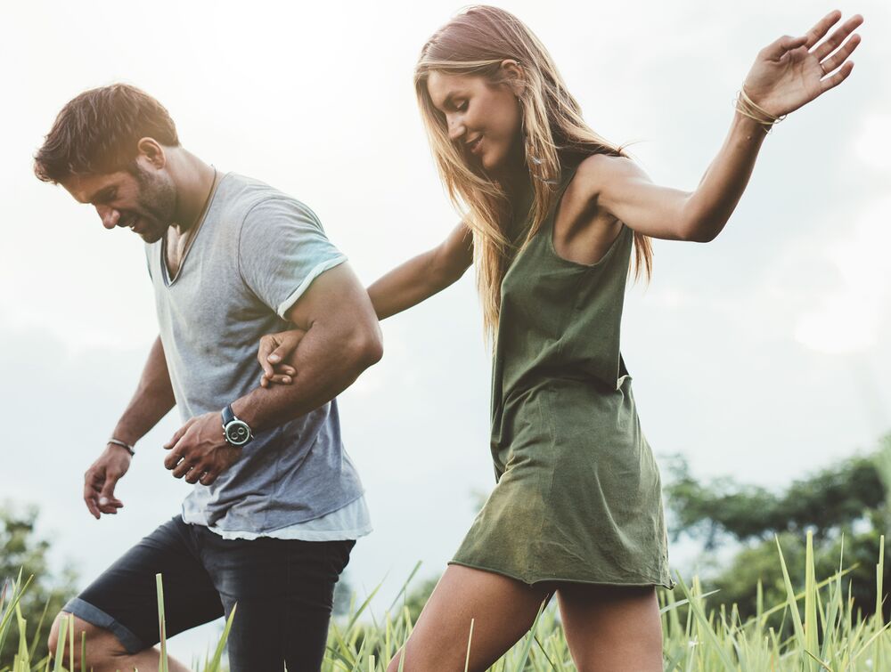 Outdoor shot of young couple walking through meadow hand in hand. Man and woman talking walk through grass field in countryside.